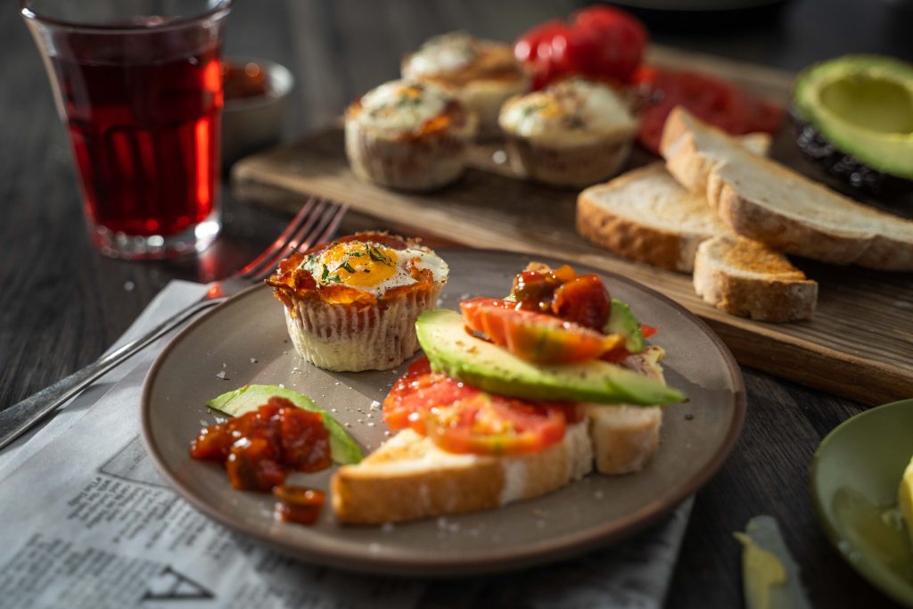 Bacon & egg cups with tomato and avocado toast on a plate with relish and a glass of juice.